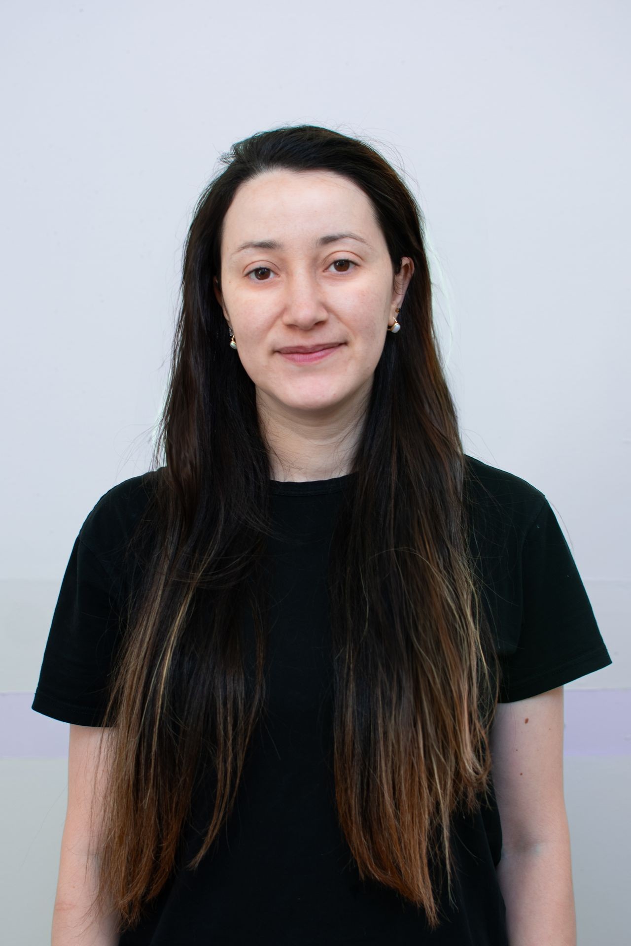 Woman with long, dark hair wearing a black shirt in front of a light-colored background.