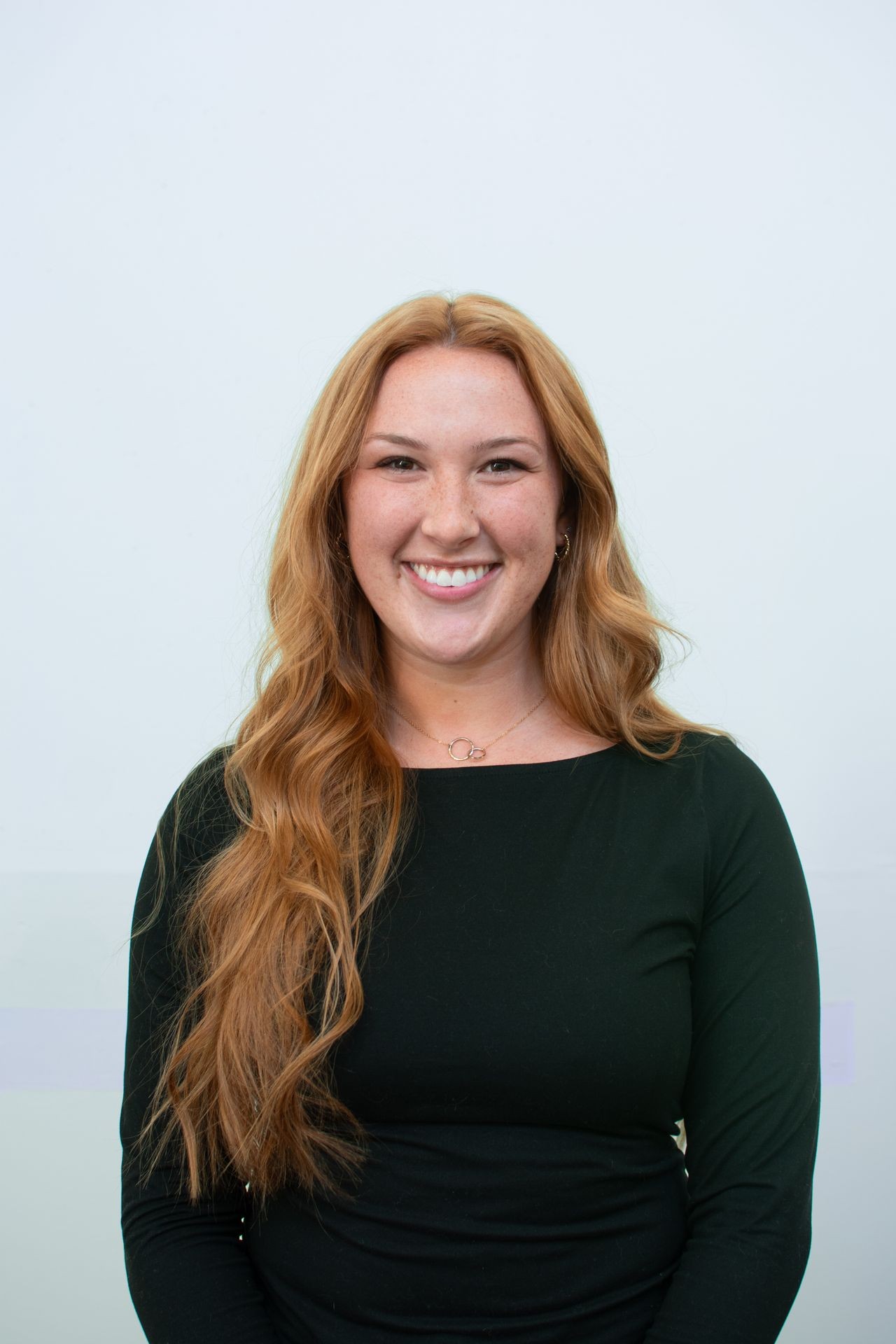 Person with long hair wearing a black top, smiling against a plain background.