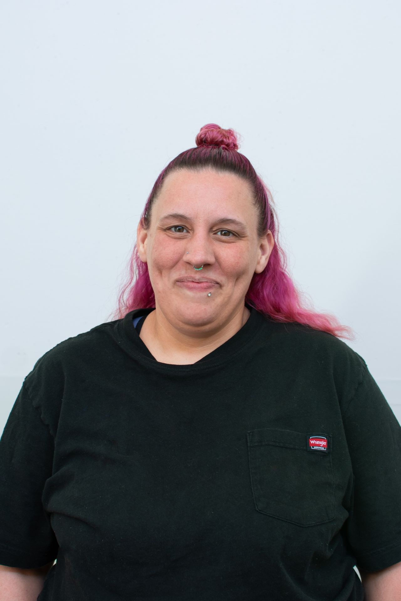 Person with pink hair in a bun, wearing a black shirt, smiling against a plain background.