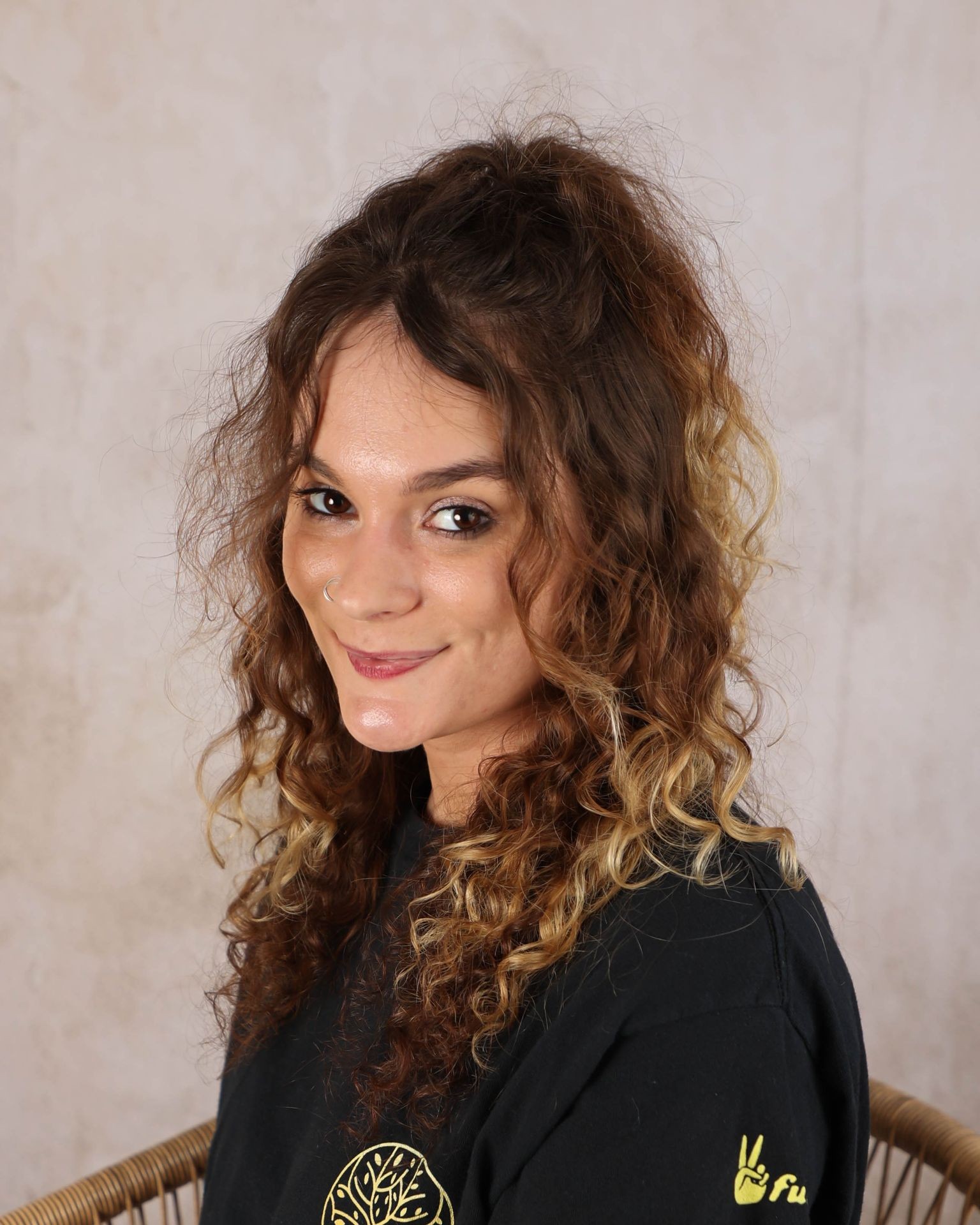 Smiling person with curly hair wearing a black shirt, seated against a light background.