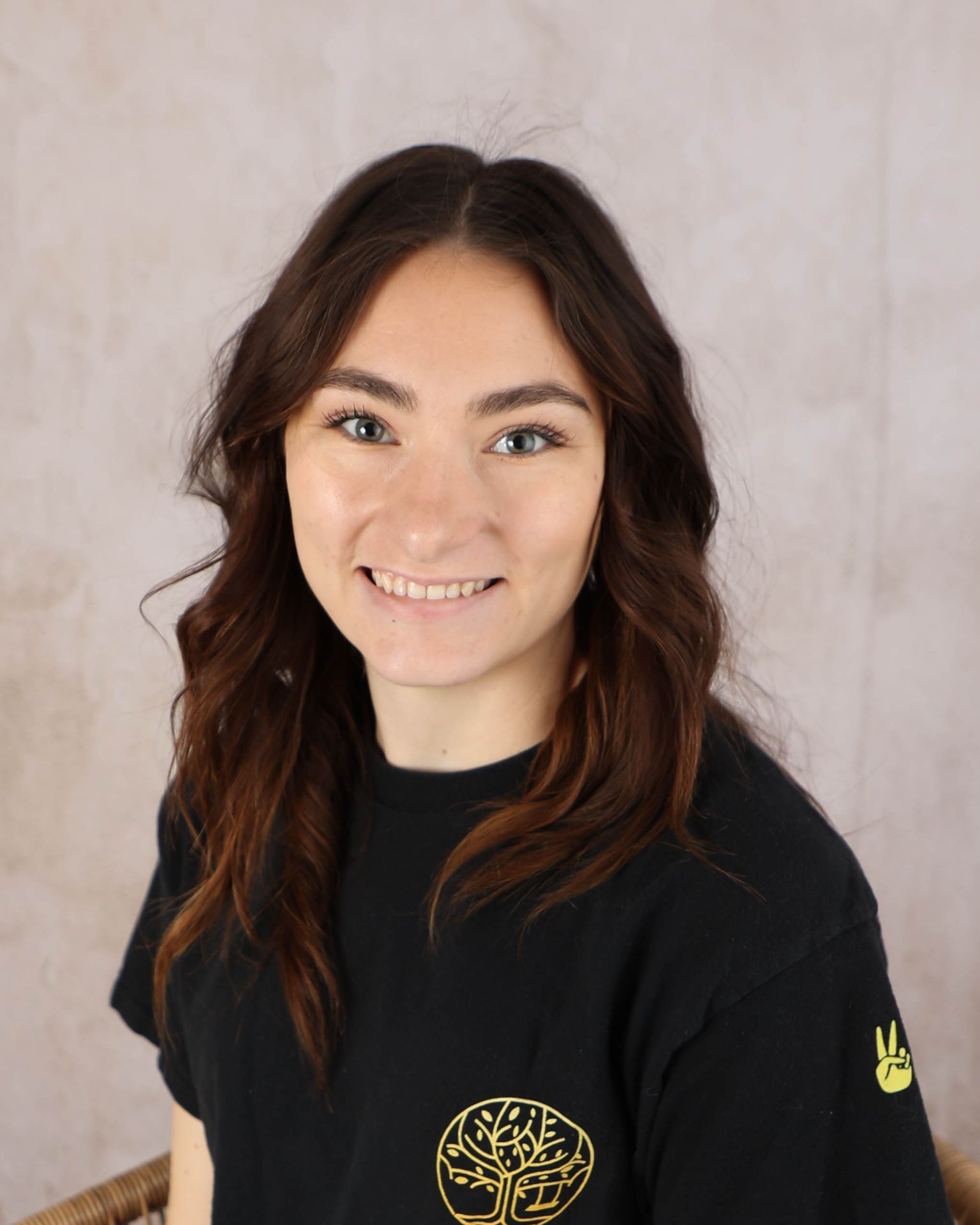 Woman with long brown hair smiling, wearing a black t-shirt with a tree logo on it.