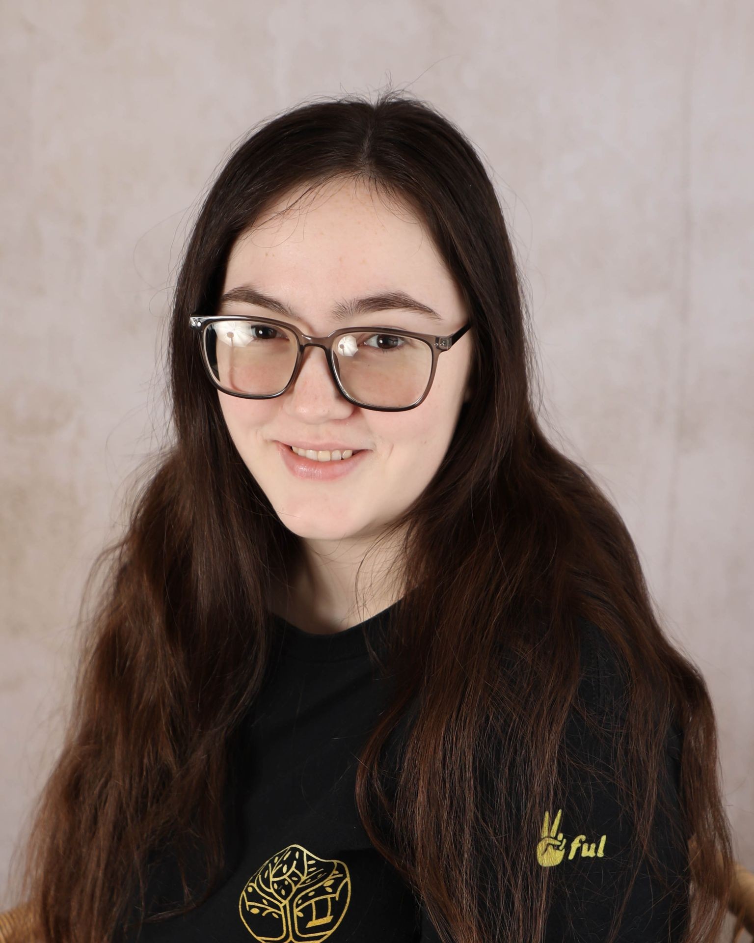 Young woman with glasses and long brown hair smiling against a neutral background.