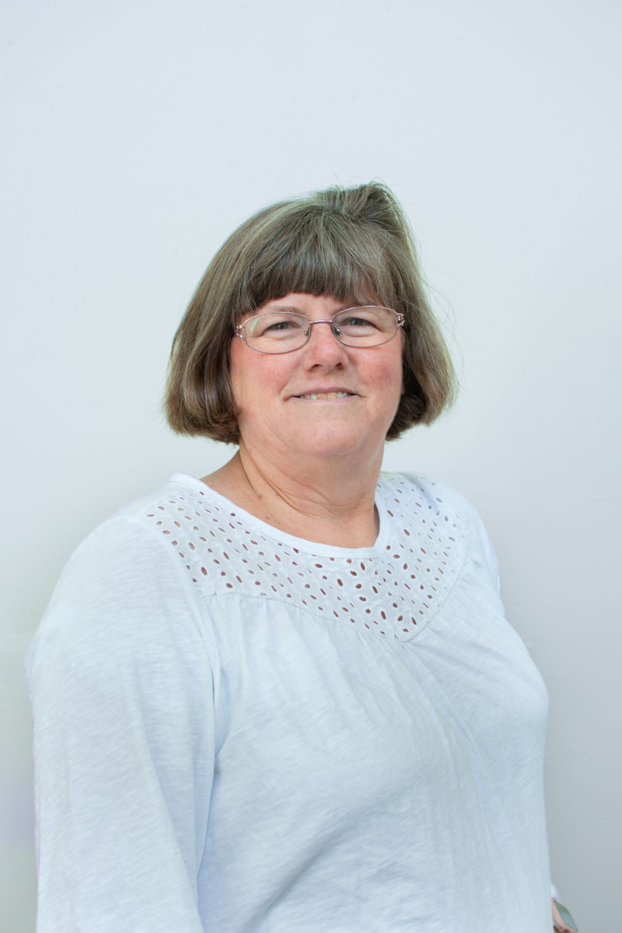 Smiling person with glasses wearing a white shirt against a light background.