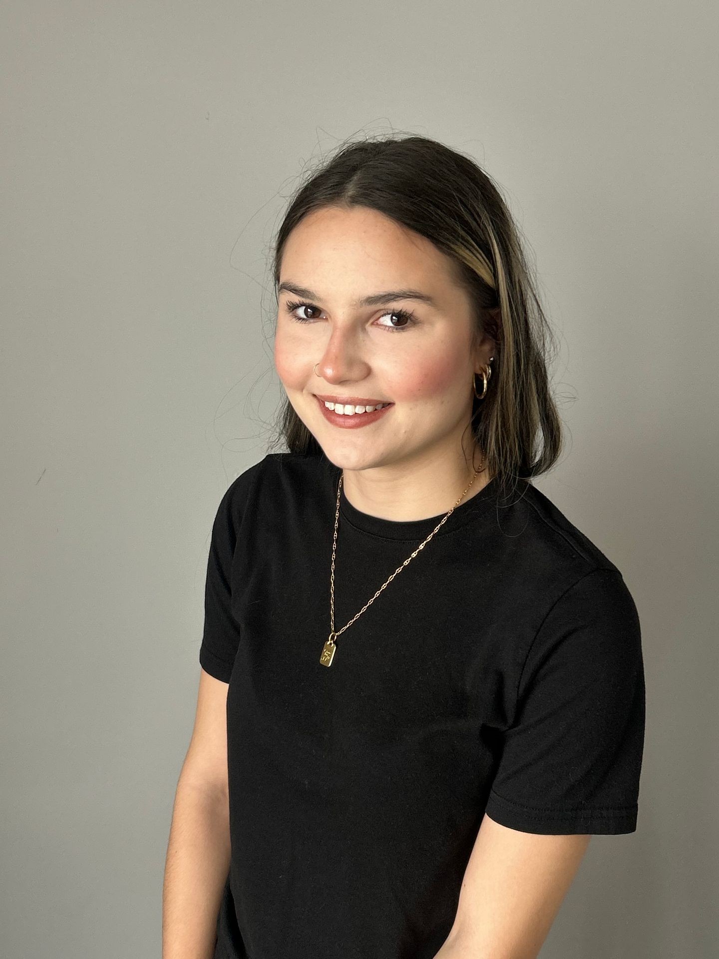 Person smiling, wearing a black t-shirt and gold necklace, against a plain background.
